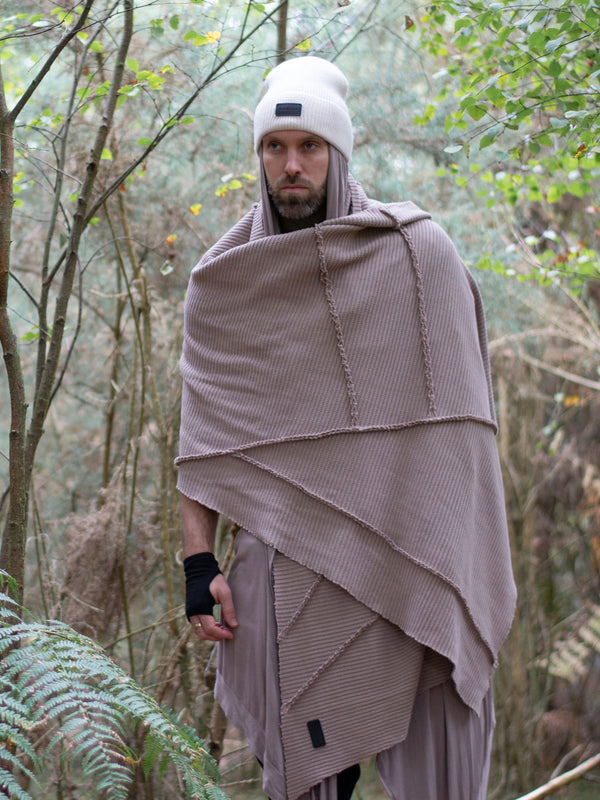 Model wearing oversized taupe knitted scarf in heavyweight knit — 250cm wrap with sculptural drape, styled as outerwear for winter layering and alternative streetwear looks.
