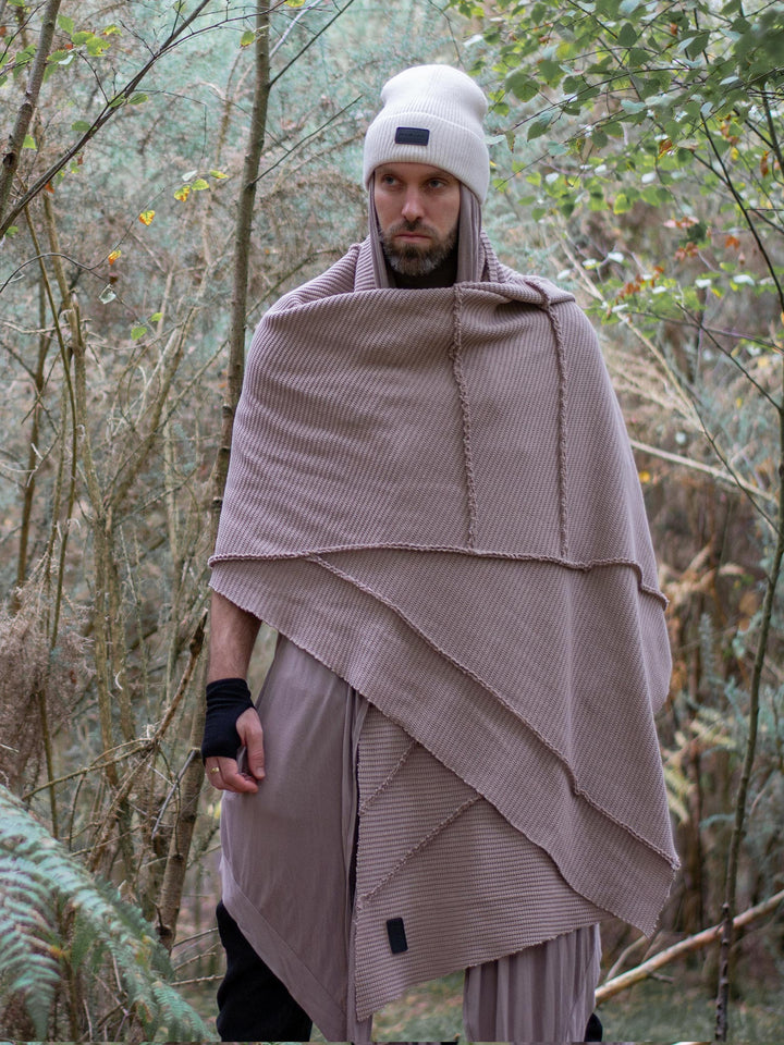 Model wearing oversized taupe knitted scarf in heavyweight knit — 250cm wrap with sculptural drape, styled as outerwear for winter layering and alternative streetwear looks.