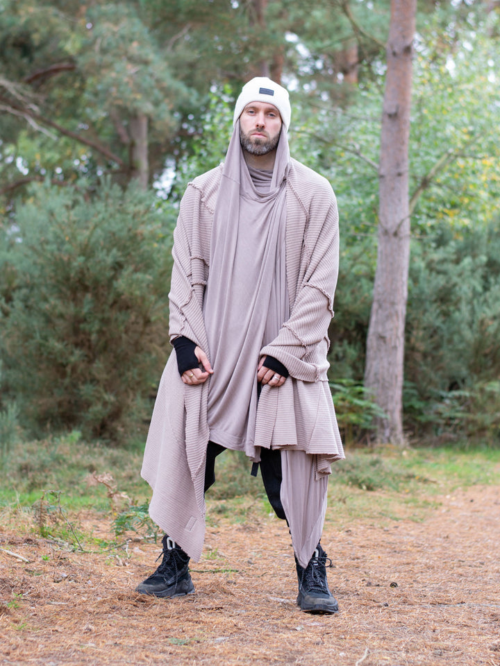 Model wearing oversized taupe knitted scarf in heavyweight knit — 250cm wrap with sculptural drape, styled as outerwear for winter layering and alternative streetwear looks.