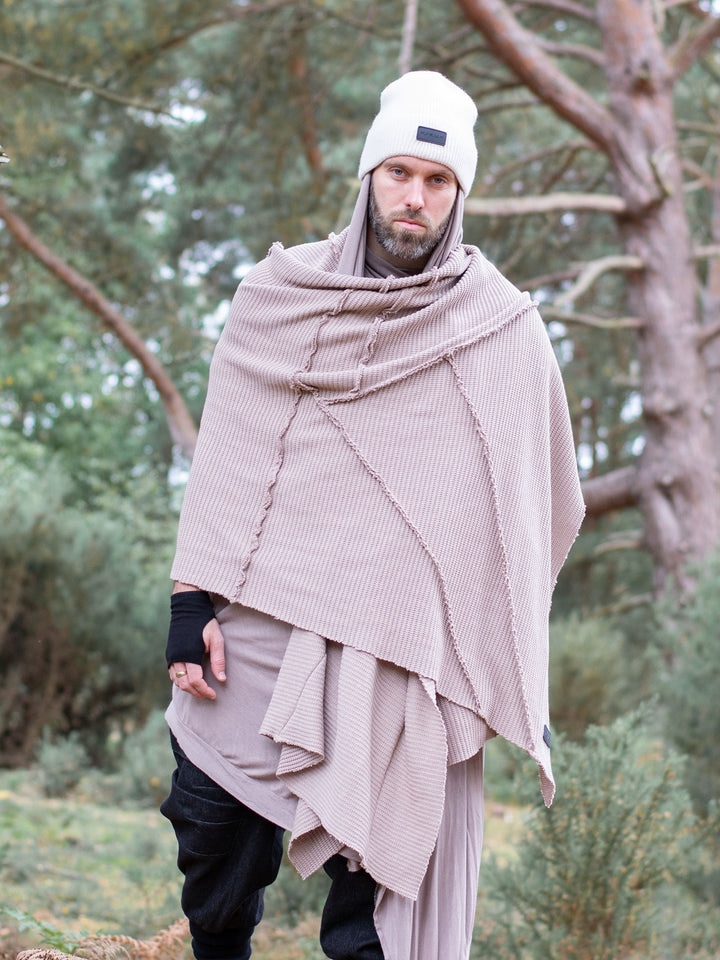 Model wearing oversized taupe knitted scarf in heavyweight knit — 250cm wrap with sculptural drape, styled as outerwear for winter layering and alternative streetwear looks.