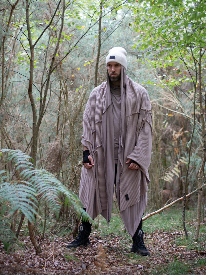 Model wearing oversized taupe knitted scarf in heavyweight knit — 250cm wrap with sculptural drape, styled as outerwear for winter layering and alternative streetwear looks.