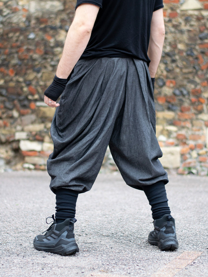 Wide-leg drop crotch ninja harem pants with voluminous pleats and tapered calf supports. Avant garde flowy mens trousers for performers, festivals or interesting looks. 