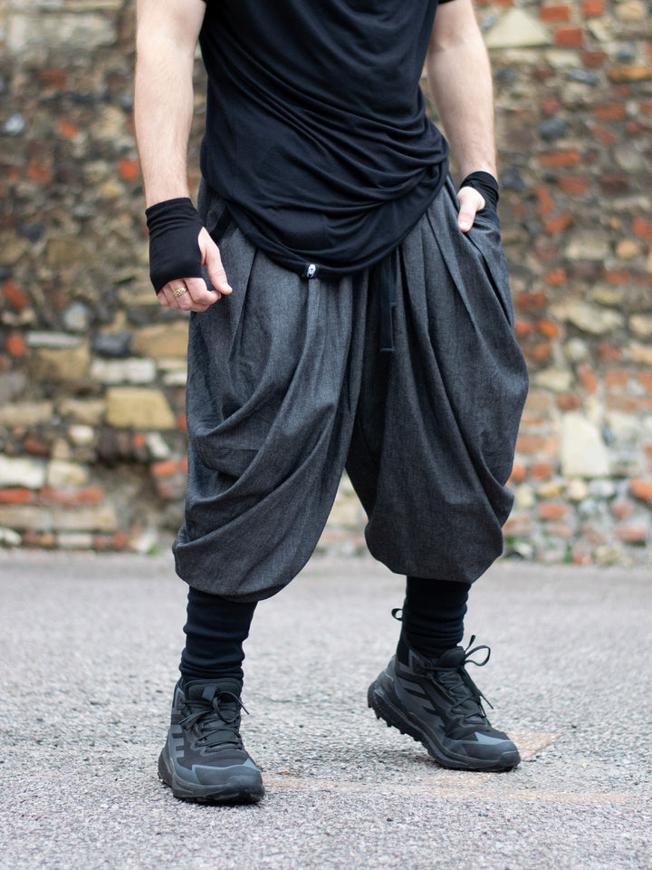 Wide-leg drop crotch ninja harem pants with voluminous pleats and tapered calf supports. Avant garde flowy mens trousers for performers, festivals or interesting looks. 