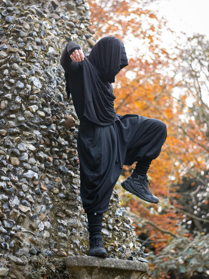 Hattori Avant Garde Ninja Pants with Drop Crotch, Japanese Style Trousers in Black - image showing the ninja pants worn outdoors in a Japanese garden by a ninja in movement