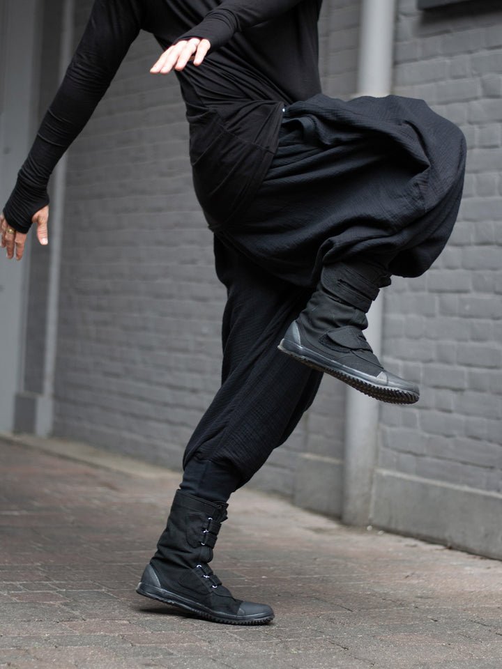 Model wearing black drop-crotch ninja pants inspired by traditional shinobi attire — Hattori harem pants in breathable muslin with pleated volume, calf supports, and a flowy, avant-garde silhouette.