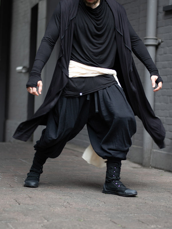 Model wearing black drop-crotch ninja pants inspired by traditional shinobi attire — Hattori harem pants in breathable muslin with pleated volume, calf supports, and a flowy, avant-garde silhouette.