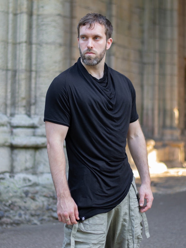 Krypt T-Shirt in black — an avant-garde, longline men’s tee made from breathable bamboo jersey. Features a draped neckline, asymmetric hem, and raglan sleeves for movement. A sculptural, apocalyptic-inspired silhouette designed for festival layering and everyday alternative styling.
