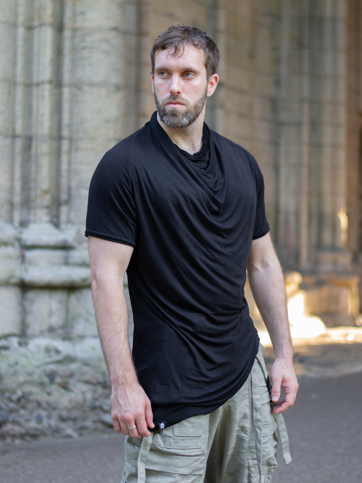 Krypt T-Shirt in black — an avant-garde, longline men’s tee made from breathable bamboo jersey. Features a draped neckline, asymmetric hem, and raglan sleeves for movement. A sculptural, apocalyptic-inspired silhouette designed for festival layering and everyday alternative styling.
