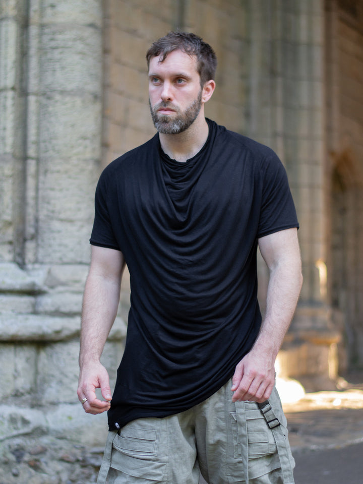 Krypt T-Shirt in black — an avant-garde, longline men’s tee made from breathable bamboo jersey. Features a draped neckline, asymmetric hem, and raglan sleeves for movement. A sculptural, apocalyptic-inspired silhouette designed for festival layering and everyday alternative styling.