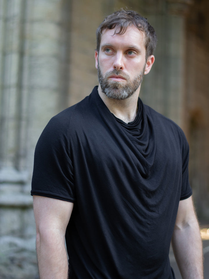 Krypt T-Shirt in black — an avant-garde, longline men’s tee made from breathable bamboo jersey. Features a draped neckline, asymmetric hem, and raglan sleeves for movement. A sculptural, apocalyptic-inspired silhouette designed for festival layering and everyday alternative styling.
