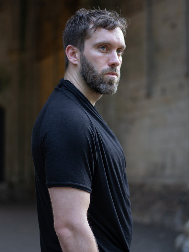 Krypt T-Shirt in black — an avant-garde, longline men’s tee made from breathable bamboo jersey. Features a draped neckline, asymmetric hem, and raglan sleeves for movement. A sculptural, apocalyptic-inspired silhouette designed for festival layering and everyday alternative styling.