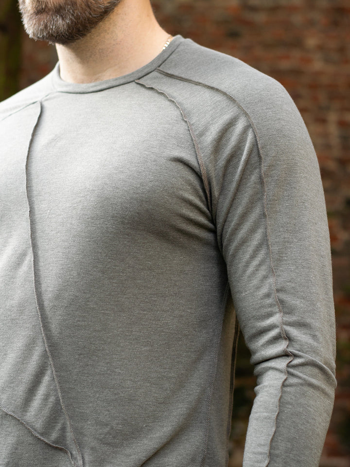 Men’s avant garde long sleeve top in Moss Grey with abstract overlock stitching, raglan sleeves, thumbholes, and longline slim silhouette. Bamboo jersey base layer - Close Up of Arm