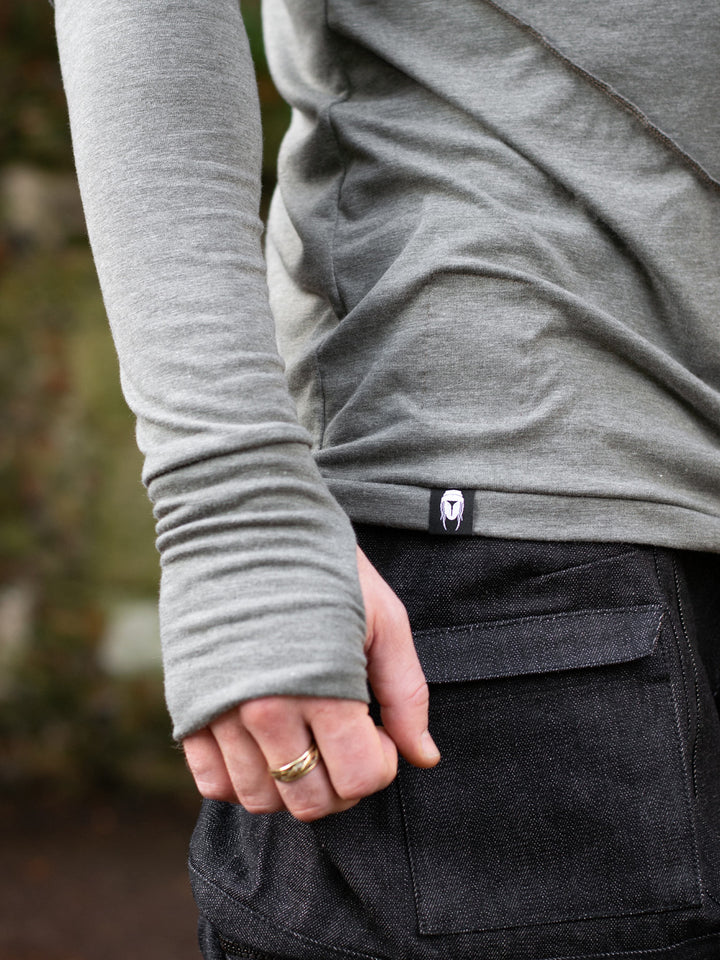 Close up of men’s avant garde long sleeve top in Moss Grey with abstract overlock stitching, raglan sleeves, thumbholes, and longline slim silhouette. Bamboo jersey base layer.