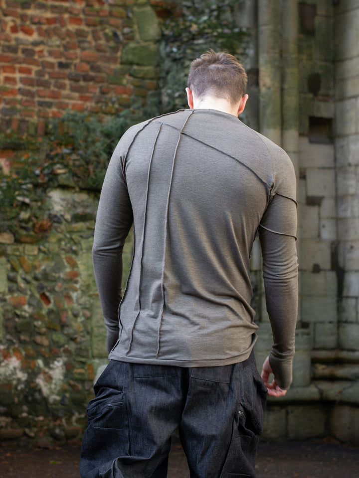 Men’s avant garde long sleeve top in Dark Taupe with abstract overlock stitching, raglan sleeves, thumbholes, and longline slim silhouette. Bamboo jersey base layer styled with techwear cargos. - Back image