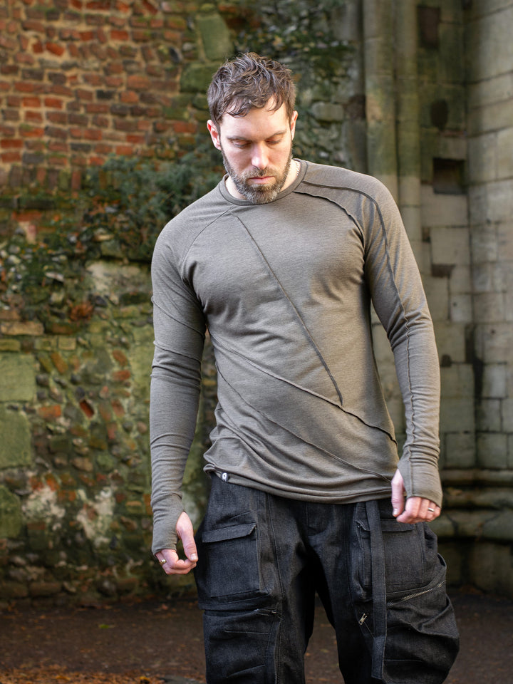 Men’s avant garde long sleeve top in Dark Taupe with abstract overlock stitching, raglan sleeves, thumbholes, and longline slim silhouette. Bamboo jersey base layer styled with techwear cargos. - Front image, model walking