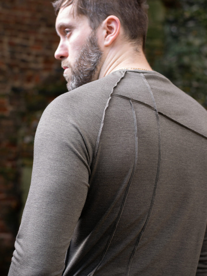 Men’s avant garde long sleeve top in Dark Taupe with abstract overlock stitching, raglan sleeves, thumbholes, and longline slim silhouette. Bamboo jersey base layer styled with techwear cargos. - Close-up of back overlock stitch