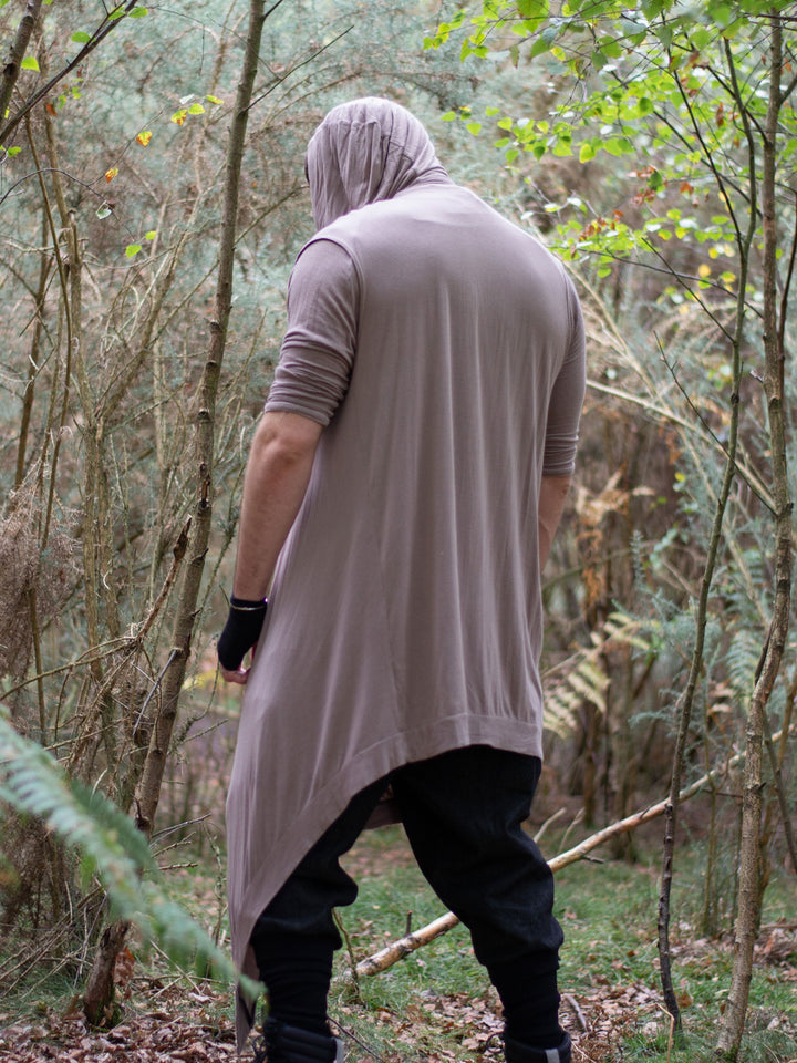 Men’s avant garde hooded cloak in sand with asymmetric wrap-over cascade design. Features bamboo jersey fabric, oversized hood, and wooden shoulder button for layered post-apocalyptic styling.