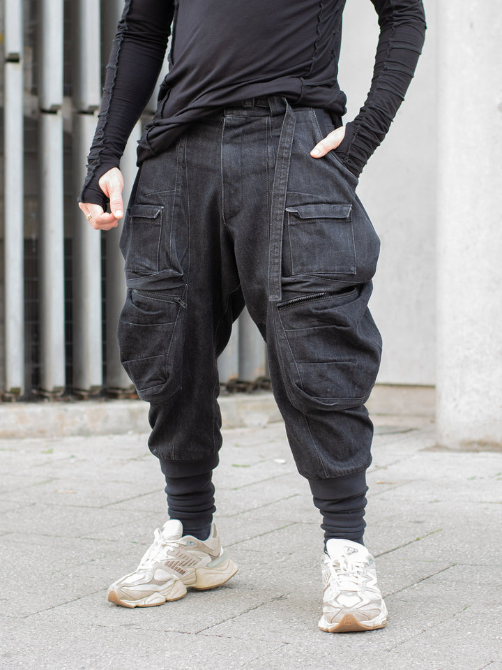 Black avant-garde cargo trousers with 10-pocket design, drop crotch fit, 15oz denim construction, metal hardware, and tactical detailing for alternative streetwear