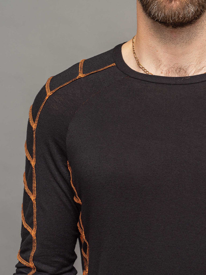 Raider dystopian avant garde men's longline tshirt in black with thumbholes and overlock contrast stitch in orange - focus on raglan sleeve